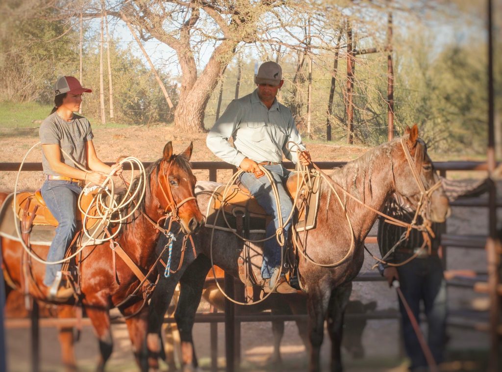 Trevor and Kaylie Haught horseback with ropes in a pen at Haught Horses and Livestock, their horse training business in Scottsdale, Arizona