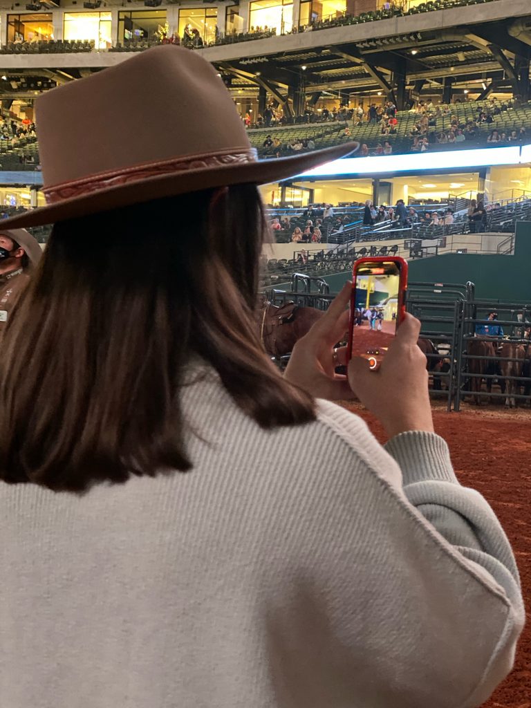 Caroline Arendt filming rodeo content on her cell phone at the NFR at Globe Life Field. 