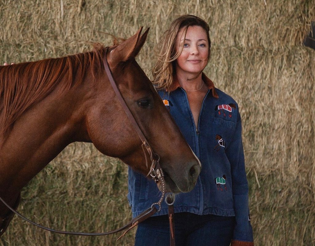 Caroline Arendt with her horse in front of stacked hay bales.