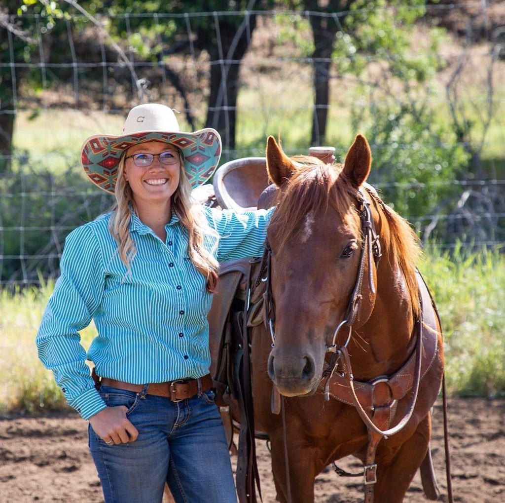Jennifer Case of Dry Creek Quarter Horses smiling beside a saddled sorrel quarter horse in a turquoise shirt and patterned hat